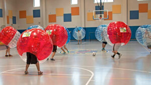 Hier spielen zwei Mannschaften in einer Halle Bubble Fußball. Eine Mannschafft trägt rote, die andere blaue Bumperz. Das Spiel auf dem Bild fand in Guantanamo statt.