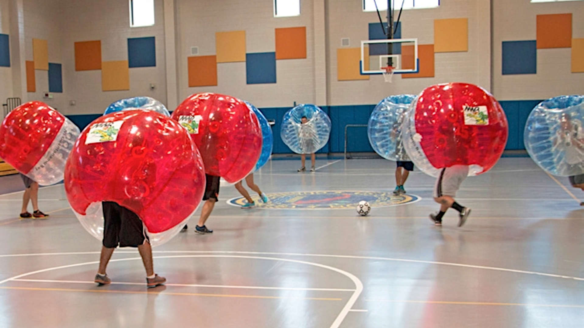 Hier spielen zwei Mannschaften in einer Halle Bubble Fußball. Eine Mannschafft trägt rote, die andere blaue Bumperz. Das Spiel auf dem Bild fand in Guantanamo statt.