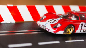 Man sieht einen kleinen Ausschnitt einer Autorennbahn von Carrera. Ein roter Rennwagen mit goldenen Felgen und der Nummer 15 kommt gerade ins Bild.