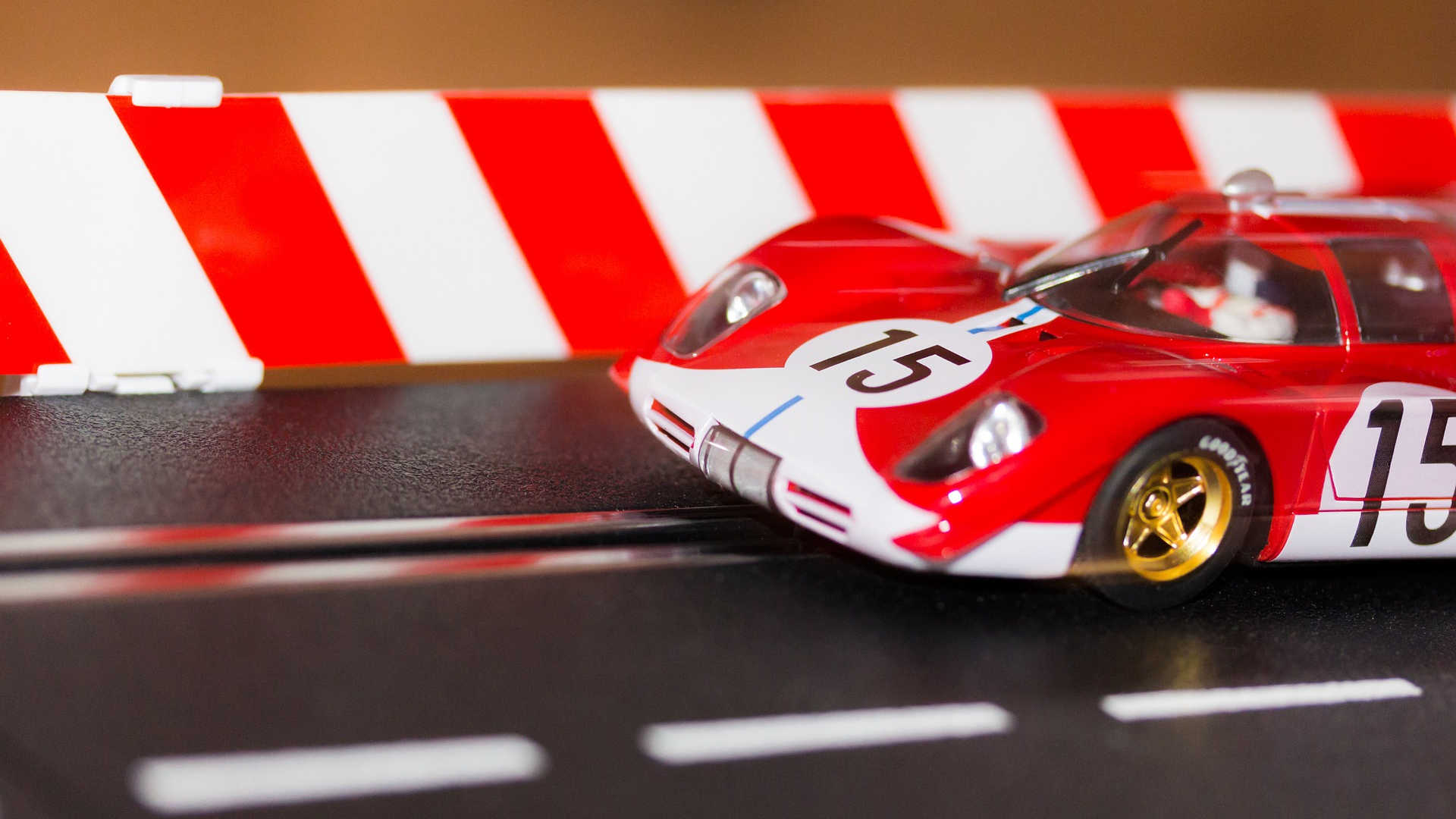 Man sieht einen kleinen Ausschnitt einer Autorennbahn von Carrera. Ein roter Rennwagen mit goldenen Felgen und der Nummer 15 kommt gerade ins Bild.