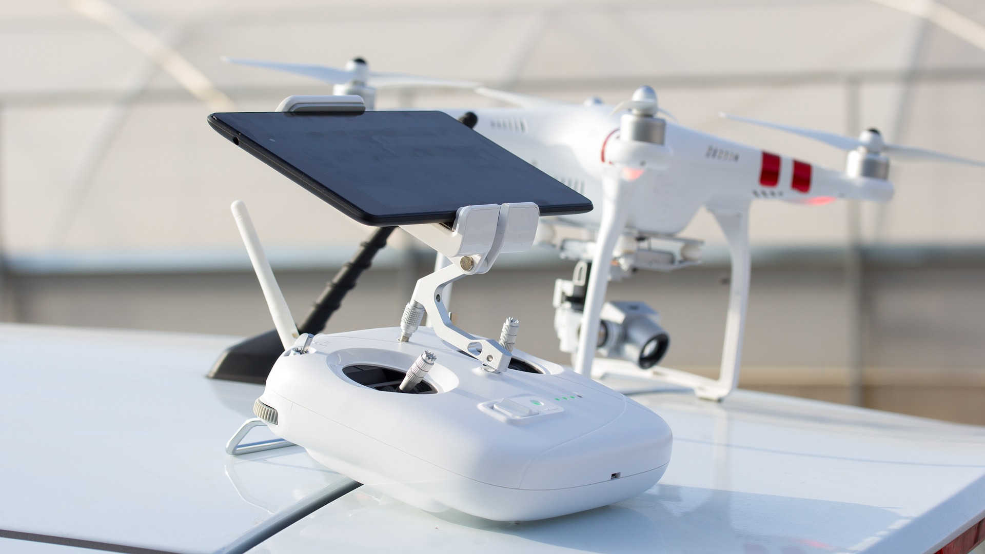 Wir sehen die Mindest-Ausstattung für FPV-Flüge – First Person View Flüge. Im Vordergrund liegt die Fernbedienung mit dem aufgesteckten Tablet als Monitor. Dahinter steht der Quadrocopter mit der Kamera.