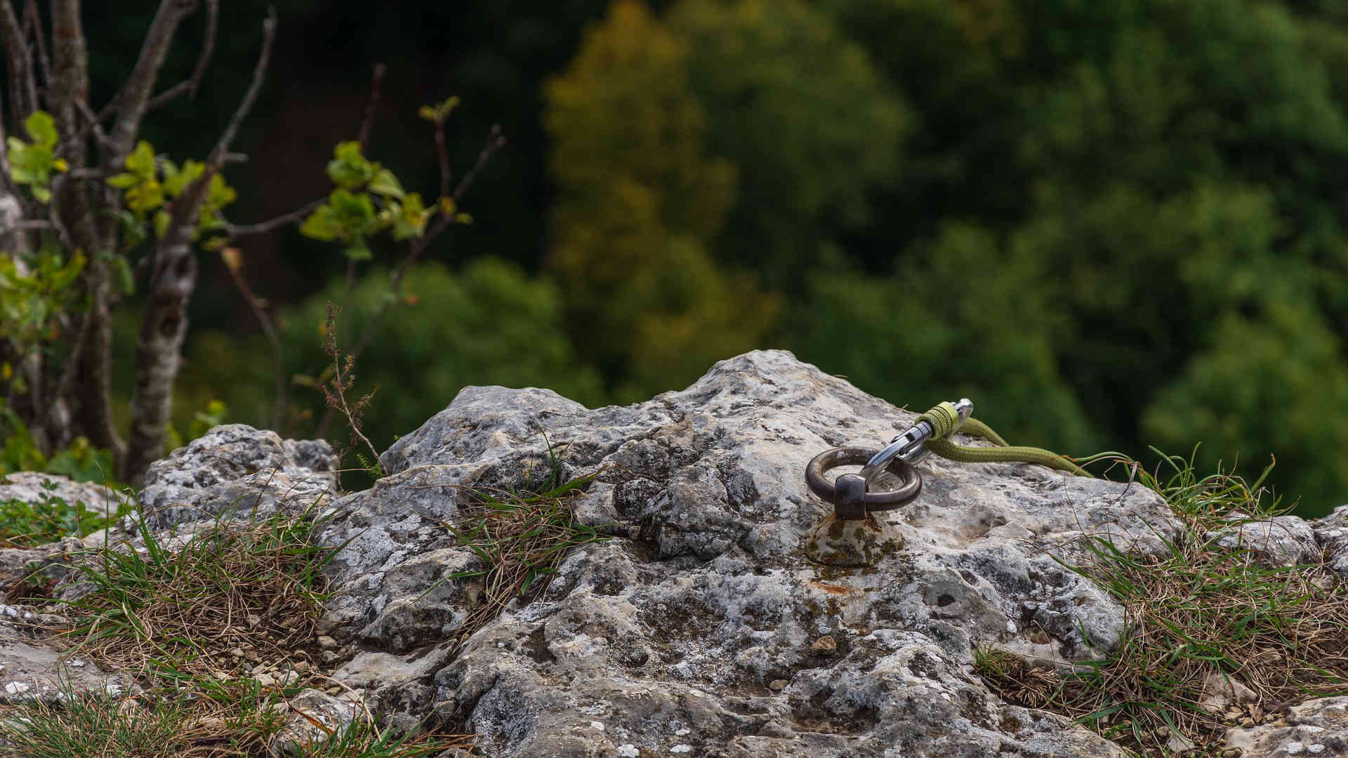 Oben am Felsen ist ein Felshaken eingeschlagen. In dessen Ring ist ein Karabinerhaken eingehängt, durch den ein Seil läuft.