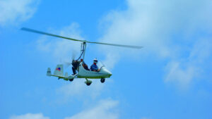 In einem Gyrocopter-Doppelsitzer sitzt ein Pilot. Er fliegt allein ohne Begleitung in einem strahlend blauen Himmel. James Bond lässt grüßen.