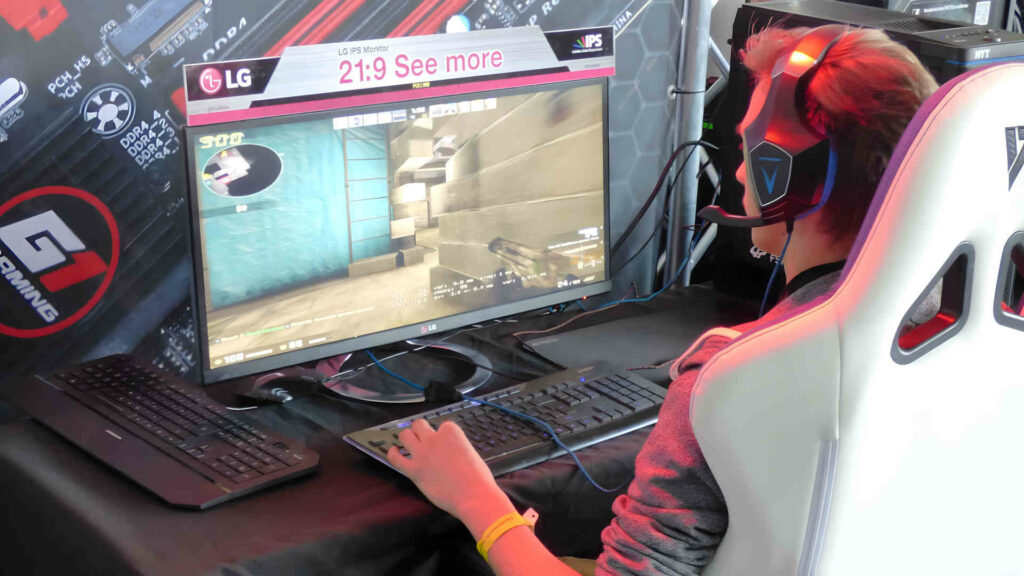 Ein junger Mann sitzt vor dem Computer und spielt. Er trägt ein Headset und ist hochkonzentriert.