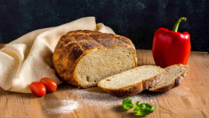 Brot backen - Ein selbst gebackenes Brot frisch angeschnitten und mit Paprika, Basilikum und Tomaten dekoriert.