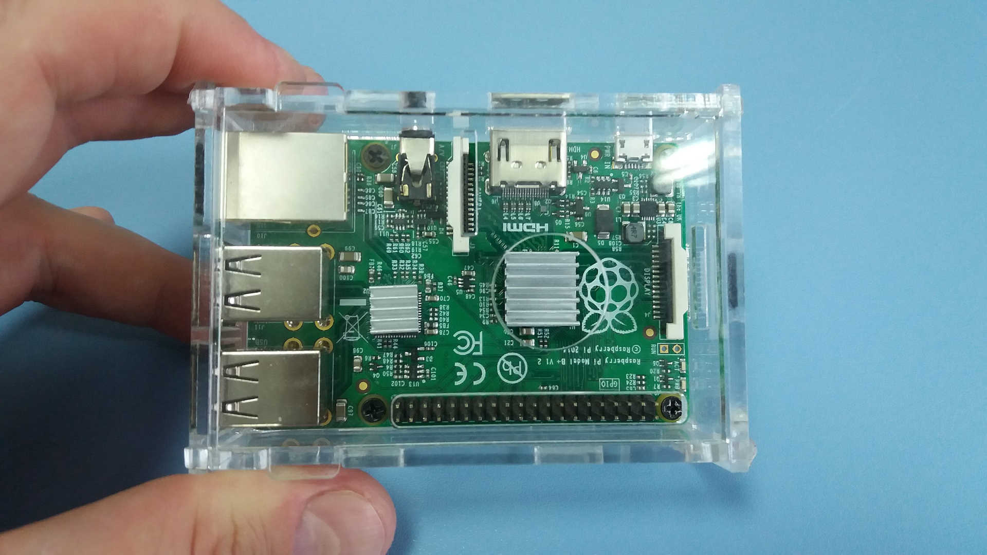 Wir sehen einen Raspberry Pi B+ in einem transparenten Gehäuse, gehalten von einer Hand. Man erkennt, wie klein den Mini-Computer ist.