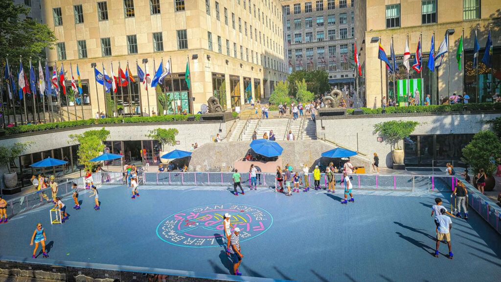 Rollschuhlaufen - Das Bild zeigt das Rockefeller Center in Midtown Manhattan, New York City. Die zentrale Fläche, die im Winter als berühmte Eislaufbahn (The Rink) dient, wird hier im Sommer als Rollschuhbahn genutzt.