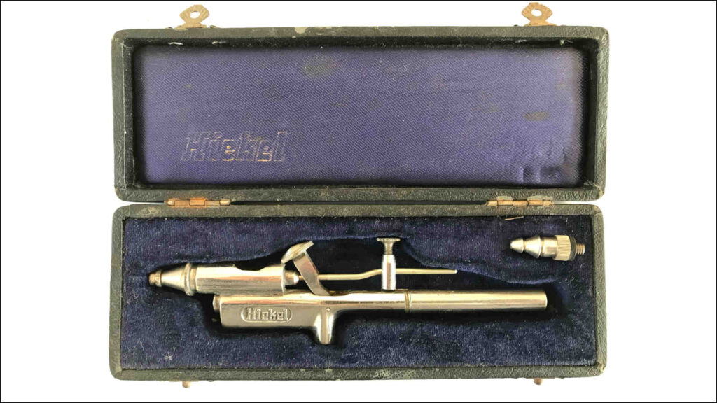 Airbrush – Wir sehen eine historische Airbrush-Pistole von der Maschinenfabrik Curt Hiekel Leipzig aus dem Zeitraum 1907 bis 1937. Es handelt sich um eine Pistole in Originalverpackung mit Zubehör.