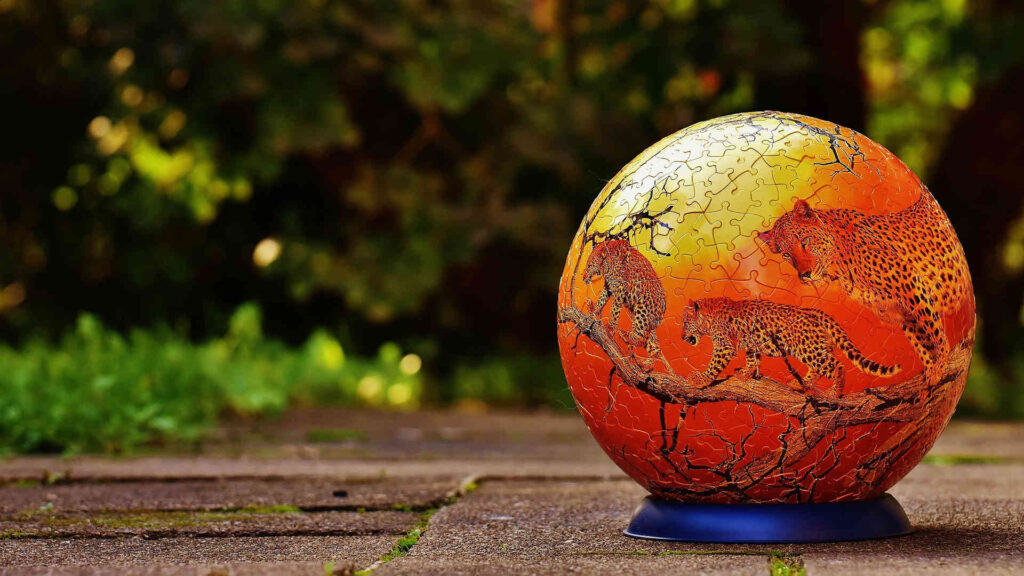 Puzzeln – Ein fertiger Puzzle-Ball als Beispiel für 3D-Puzzles. Mehrere Leoparden, die auf Bäumen klettern, sind hier als Motiv gewählt.