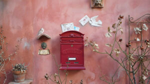 Brieftauben – Ein roter Briefkasten an einer mittels Wischtechnik verzierten Wand. Symbolisch bringt eine auf die Wand gezeichnete Brieftaube einen Brief.