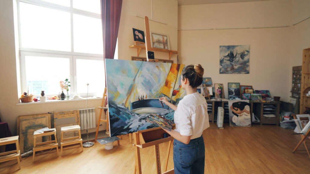Ölmalerei – Eine Frau steht im Atelier vor der Staffelei und malt.