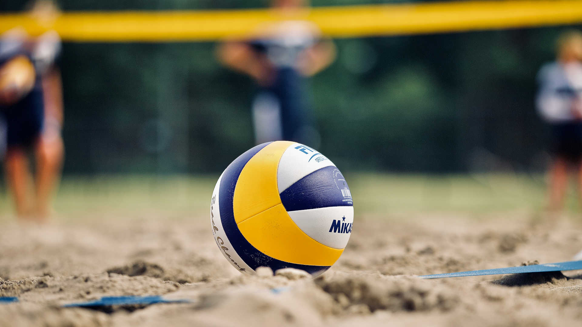 Beachvolleyball – Ein Beachvolleyball der Firma Mikasa mit dem typisch geschwungenen 10-Panel-Muster in Blau, Gelb und Weiß. Auf der Seite sind der Schriftzug Mikasa, das FIVB-Logo sowie der Schriftzug "Beach Champ" zu sehen.
